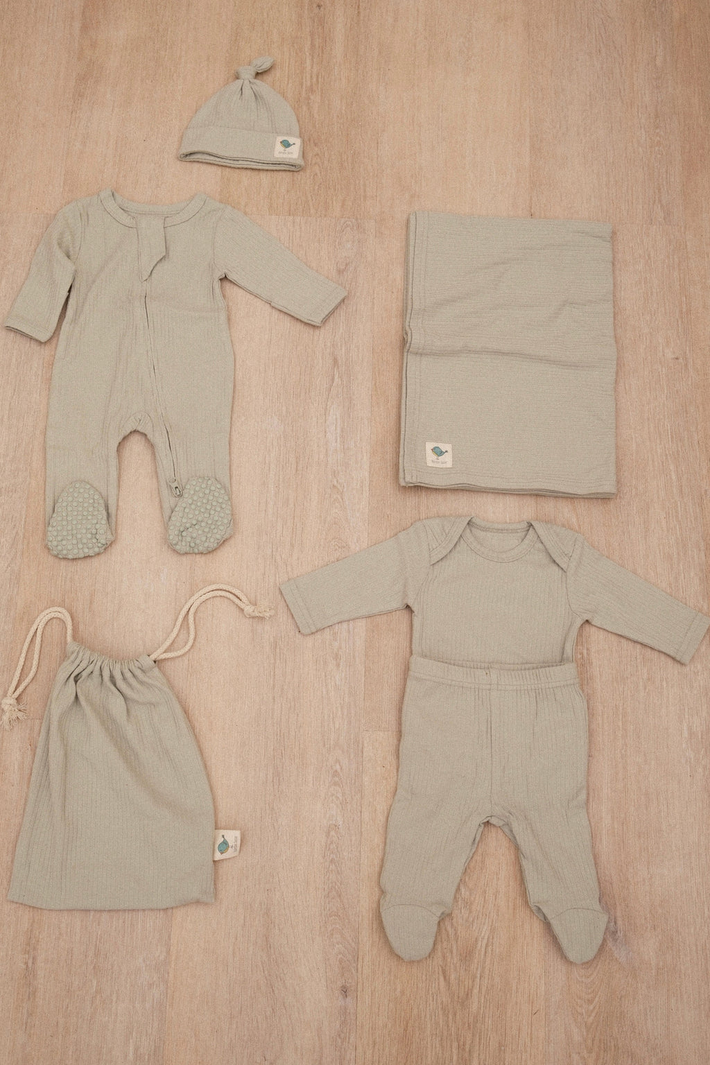 Baby clothing set with two rompers, a hat, and a blanket on a wooden surface.